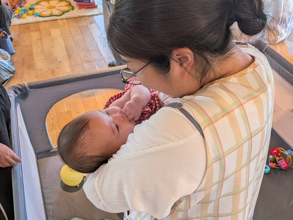 Mama's marche（谷川建設 大村住宅展示場）の託児コーナーで、スタッフが赤ちゃんを抱っこしてあやしている様子