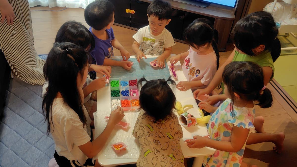 親子イベントで、子どもたちがテーブルを囲んで色とりどりのビーズの工作をしている様子